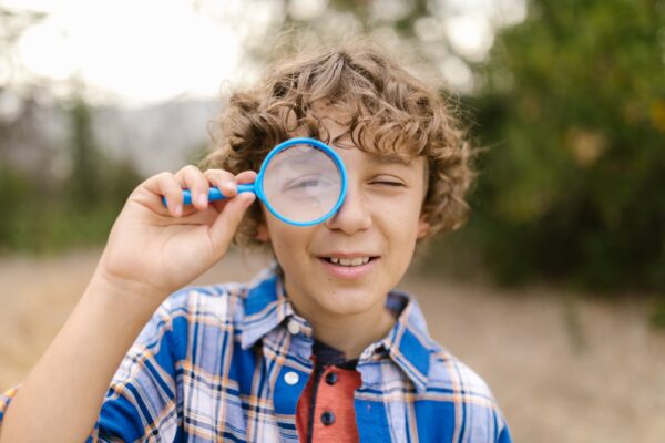 boy with curly hair looking through a magnifying glass on his one eye